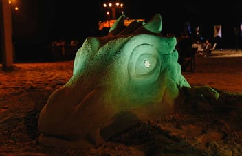 Une sculpture de sable vert lumineuse représentant une tête de dragon sur une plage, la nuit, lors d'un événement en plein air.
