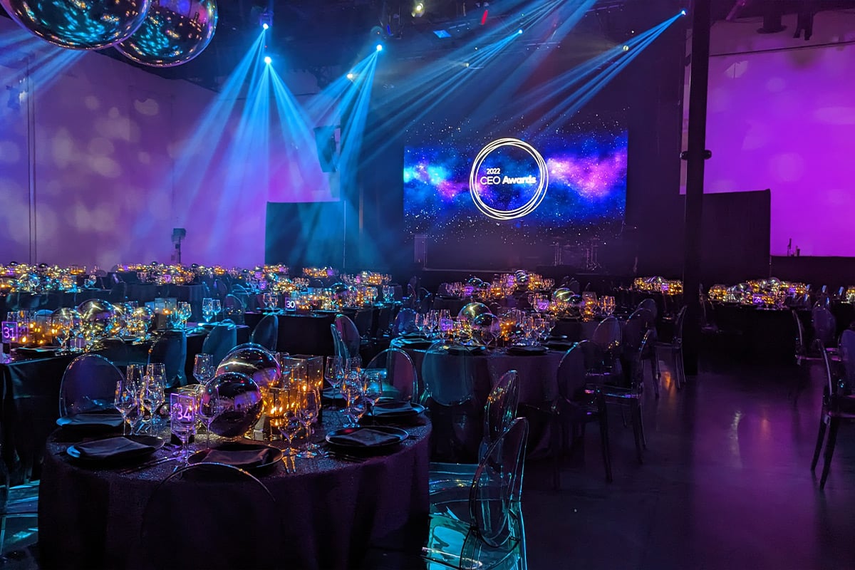 Salle de bal élégante avec un éclairage bleu spectaculaire, une boule à facettes et des tables de repas formelles préparées pour la cérémonie de remise des prix.