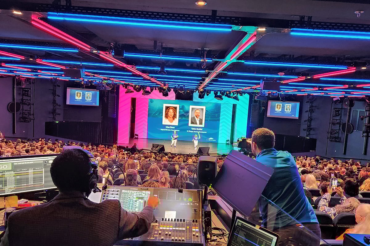 Audience regardant une présentation avec des néons et des écrans dans un théâtre