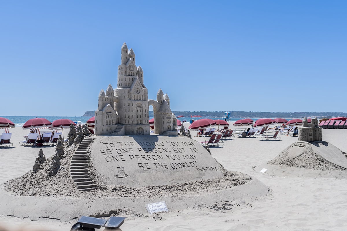 Château de sable élaboré avec des tours et un message gravé sur une plage ensoleillée avec des parasols roses